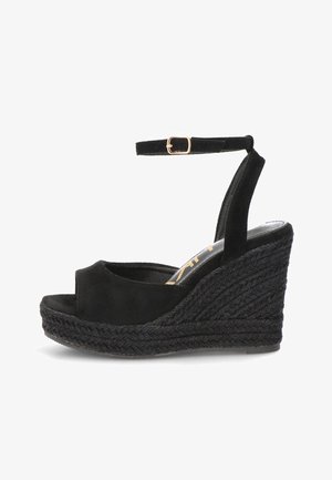 Sandalia de cuña de ante negro con suela plataforma trenzada y correa al tobillo con hebilla dorada, diseño de punta abierta.