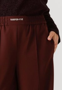 Pantalon bourgogne avec une taille élastique portant l'étiquette "HARPER&YVE", doté de poches latérales et d'une texture de tissu lisse.