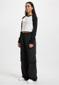 White and black long-sleeve crop top with logo, paired with black cargo pants featuring side pockets, and white sneakers.