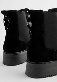 Mustad suede säärebootsid elastsete külgpaneelidega, hõbedaste detailidega ja klumpneil, millel on tekstuuriga sooned.