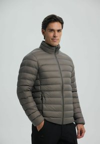 Grå pufferjakke med horisontale quiltede sektioner, høj krave og frontlynlås. Materialet har en glat, reflekterende tekstur.