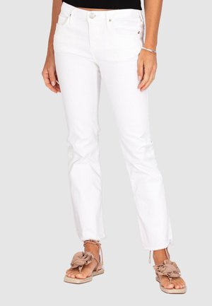 Weiße Denim-Jeans mit schlankem Schnitt und fransigem Saum, ausgestattet mit einem Knopfverschluss und vorderen Taschen, kombiniert mit beige Sandalen mit dekorativen Schleifen.