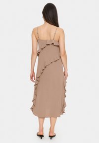Rochie midi maro cu bretele subțiri, având accente volanase pe laturi. Țesătură netedă cu o textură fluidă și o croială lejeră.