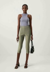 Ανοιχτό γκρι εφαρμοστό μπλουζάκι συνδυασμένο με ελιές πράσινα cropped παντελόνια. Το μοντέλο κρατά μια μικρή μαύρη τσάντα, φορώντας μαύρες ψηλοτάκουνες σαγιονάρες.