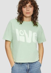 Miętowa, krótka koszulka z miękkiej bawełny, z wyraźnym białym nadrukiem "LOVE", krótkimi rękawami i luźnym fasonem.