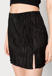Saia mini pregueada preta com um cós elástico, apresentando uma abertura lateral e uma textura lisa e brilhante.