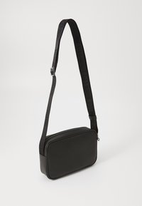 Black synthetic leather crossbody bag with a rectangular shape, zip closure, and a textured strap featuring the brand name.
