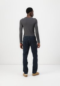 Camisa gris de manga larga ajustada con costuras en contraste; combinada con jeans oscuros ajustados, que cuentan con bolsillos traseros y un distintivo de cuero.