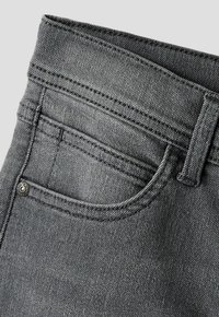 Primer plano del bolsillo de un vaquero gris con costuras visibles, trabilla para el cinturón y pequeño remache de metal en la esquina del bolsillo.