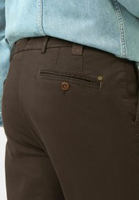 Pantalon marron avec une poche arrière à fermeture bouton, texture de tissu lisse et un détail de couture discret près de la taille.