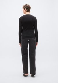 Fekete hosszú ujjú felső kerek nyakkivágással, magas derekú, sötétszürke bő szárú farmerral párosítva. Sima textúrájú, szabott részletekkel.