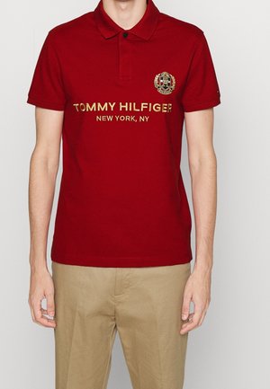 Rotes Polohemd aus Baumwolle mit einem Kragen, verziert mit goldbesticktem Schriftzug "TOMMY HILFIGER NEW YORK, NY" und einem Logo-Patch auf der Brust.