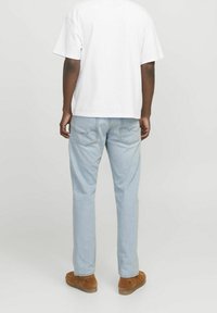 Jeans de denim en azul claro con un corte relajado, que cuentan con dos bolsillos traseros y costuras en contraste, combinados con una camiseta blanca lisa y zapatos marrones.