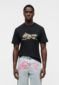 Μαύρο βαμβακερό μπλουζάκι με παραλλαγής γραφικό ενός λύκου. Ανοιχτό μπλε τζιν με ροζ ζωγραφιά ζώου στη πίσω τσέπη.