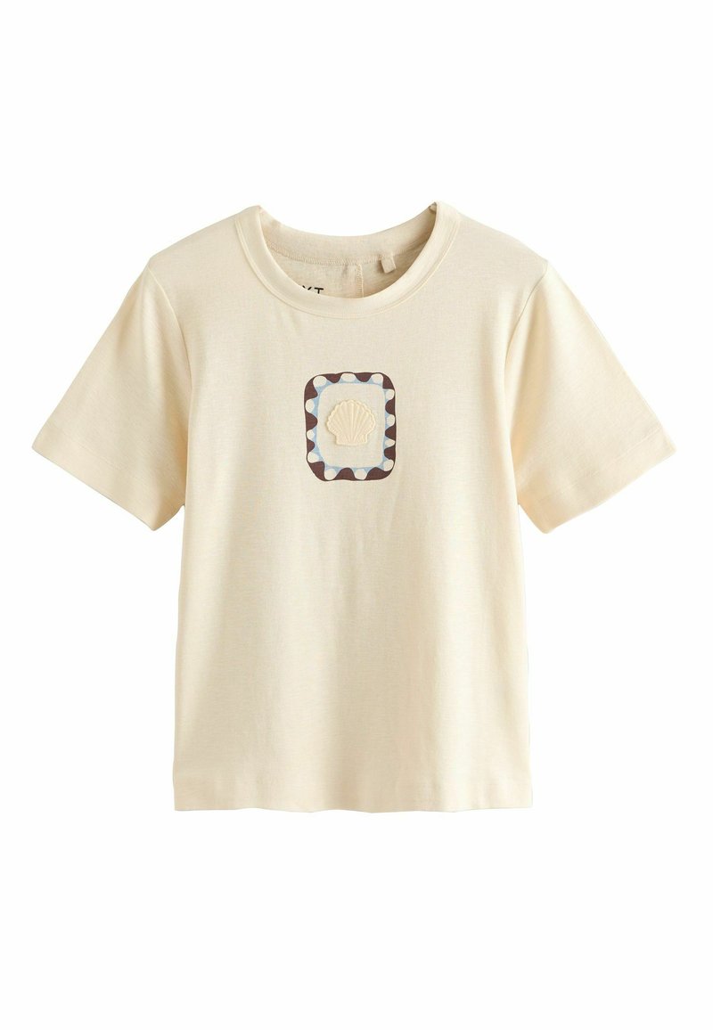 T-shirt beige à manches courtes avec un écusson de coquillage centré encadré par une bordure festonnée bleue et marron sur la poitrine.