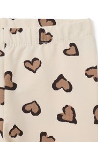 Tissu beige avec des formes de cœur marron éparpillées et bordées de noir, présentant une taille élastique en haut.