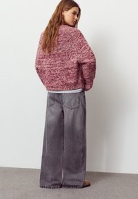 Pulover roz gros din tricot cu un model texturat, asortat cu blugi gri cu picioare largi, buzunare în spate și tiv destrămat.