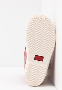 Baskets rouges avec semelle en caoutchouc blanche présentant un motif en chevrons, petite étiquette rouge, et "Fabriqué en Espagne" embossé au fond. Taille 26.