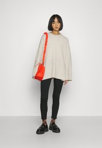 Beige oversized stickad tröja med ribbad särkant, i kombination med svarta leggings och kraftiga svarta skor. Accessoarer med en klar röd dragsko-väska.