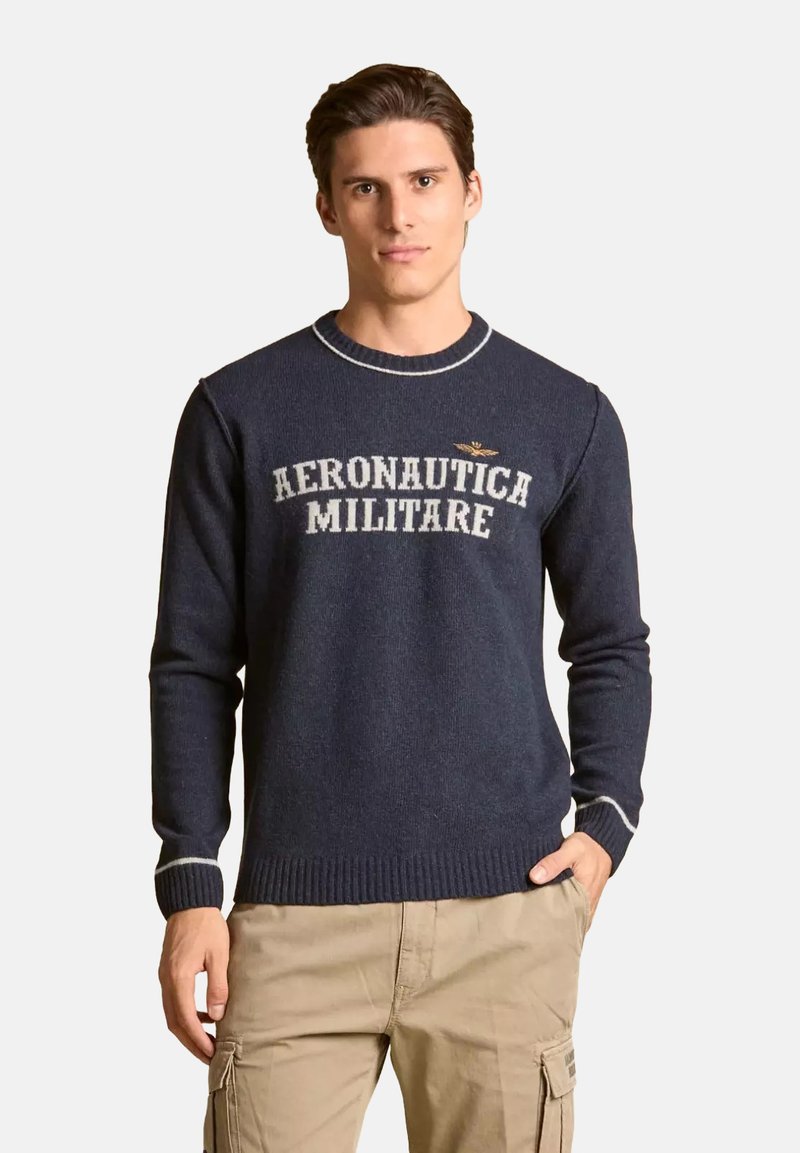 Maglione della marina realizzato in tessuto a maglia con polsini e orlo a coste. Caratterizzato dal testo "AERONAUTICA MILITARE" in bianco e un piccolo logo sopra.