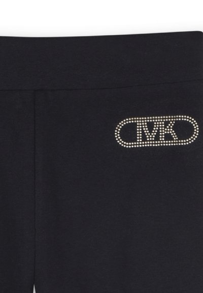 Des leggings noirs présentent un logo orné de cristaux à la taille, mettant en avant un design élégant et stylé.
