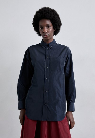 Chemise bleu marine en matière légère, avec un col boutonné, des manches longues et une poche poitrine, offrant une coupe décontractée.