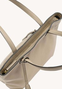 Sac fourre-tout en cuir beige avec une texture lisse, fermeture zippée en haut et bordure noire contrastante. Dispose de deux poignées et d'un intérieur spacieux.