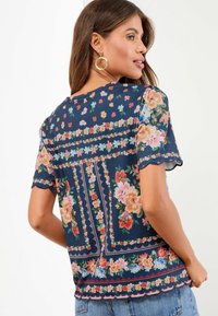 Blouse à manches courtes à motif floral bleu marine, avec des bords festonnés et des coutures détaillées, ornée de fleurs de différentes couleurs.
