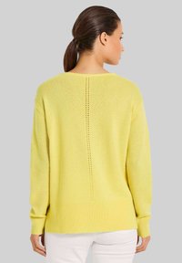 Gelbes Strickpullover mit lockerer Passform, gerippten Bündchen und Saum sowie einer vertikalen Linie aus offenen Maschen auf der Rückseite.