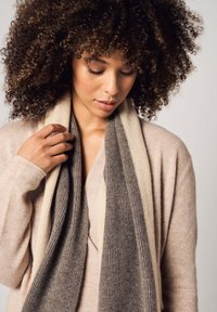 Sciarpa lavorata a maglia con sezioni rigate grigie e beige, caratterizzata da una texture morbida. Indossata in modo stiloso attorno al collo, abbinata a un pullover leggero.