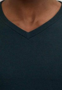 Dunkelgrüner, gestrickter V-Ausschnitt-Pullover mit strukturiertem Finish und geripptem Ausschnitt, der eine enganliegende Passform zeigt.