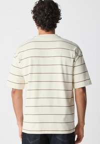 Korte mouwen shirt in crème met bruine horizontale strepen, gemaakt van zachte stof; ontspannen pasvorm met een ronde hals en verlaagde schouders.
