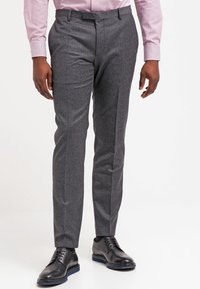 Graue maßgeschneiderte Hose aus strukturiertem Stoff, mit schmaler Passform, Seitentaschen und flacher Vorderseite, kombiniert mit schwarzen Anzugschuhen.