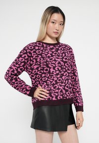 Maglione leopardato viola e rosa con colletto rotondo, maniche lunghe e polsini a costine, abbinato a una mini gonna in pelle nera.
