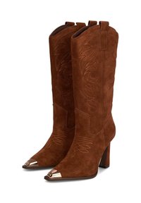 Stivali al ginocchio in suede marrone con punta affusolata. Presentano cuciture decorative e una punta metallica. Dotati di un tacco spesso e linguette laterali.