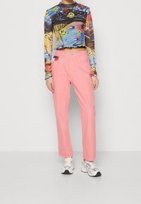 Camiseta de manga larga de colores múltiples con estampados de caras sonrientes, combinada con pantalones rectos de color rosa claro y zapatillas blancas con acentos grises.