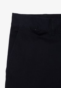 Pantaloni in denim blu scuro con taglio dritto, tasche standard e parte anteriore piatta, con una texture liscia e dettagli cuciti.