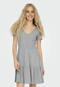 Grå klänning med kort ärm och V-ringning, texturerad tyg, åtsittande bodice och utsvängd, veckad kjol. Utsmyckning med scalloped fåll i botten.