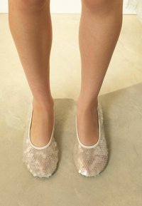 Caurspīdīgas gaismas rozā baleta kurpes ar apaļām spīdīgām aplikācijām, ar mīkstu zolīti un plānu, baltu apmali ap atvērumu.