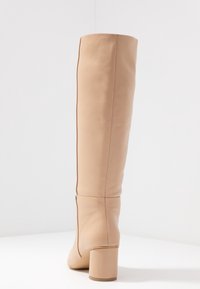 Knee-high beige leather boots with a smooth texture, block heel, and a fitted design. Seam details visible on the side.