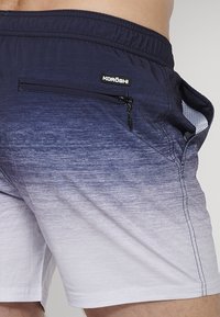 KORÖSHI plavky v námorníckej modrej s bielym prechodom, s elastickým pásom, zipsovou bočnou vreckom a sieťovinou pre lepšiu priedušnosť.