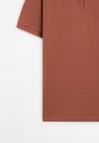 Polo manches courtes couleur rouille avec tissu texturé, manches à ourlet plat et coutures simples et propres sur fond blanc.
