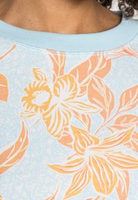Tejido azul claro con un estampado floral en naranja y crema. Escote redondeado con ribete acanalado. Textura suave, elementos de diseño tropical.