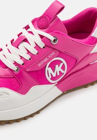 Baskets Michael Kors rose vif et blanche avec lacets blancs, emblème du logo sur le côté et semelle en caoutchouc texturée sur fond blanc.