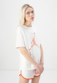 White cotton T-shirt featuring an orange floral Jordan logo. Paired with white shorts trimmed in orange. Simple, relaxed fit design.