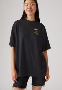 Black oversized t-shirt made from cotton, featuring a yellow sun graphic and "LEVI'S" text on the chest. Short sleeves and a round neckline.