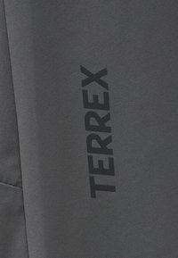 Σκούρο γκρι ύφασμα με την λέξη «TERREX» τυπωμένη κάθετα με μαύρα γράμματα σε υφή επιφάνειας.