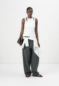 White sleeveless top with shoulder straps, grey wide-leg pants, and a knotted white layer. Black clutch and flat sandals complete the outfit.
