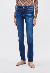 Mėlyni ploni džinsai iš džinsinio audinio, su vidutinio aukščio liemeniu, subtiliu išblukimu ir klasikiniu penkių kišenių dizainu. Derinami su tekstūruotomis mule bateliais.