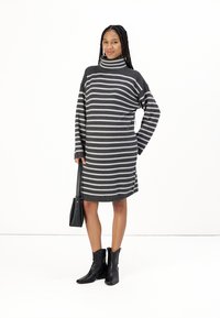 Robe pull grise avec des rayures horizontales blanches, col montant, manches longues et coupe décontractée, associée à des bottes chelsea noires et un sac à main.